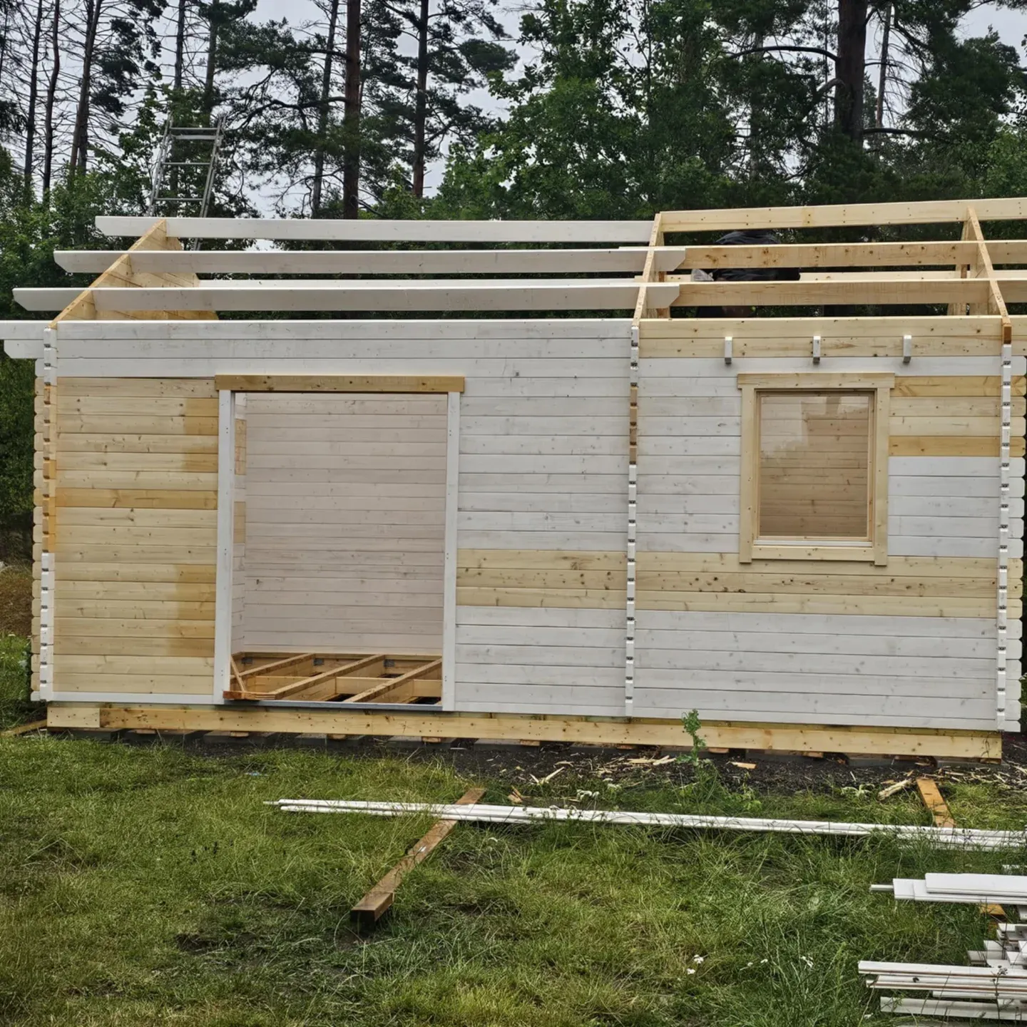 Sidovy av knuttimrad byggnad med stege och material på marken